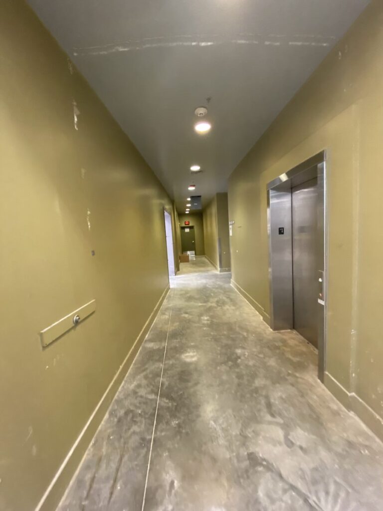 Completed hallway with painted walls, finished ceilings, recessed lighting, and retail back-of-house access areas