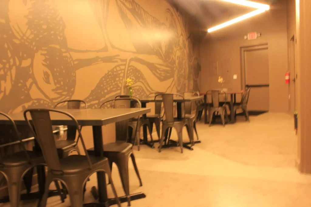 A restaurant patio featuring tables and chairs set against a colorful mural backdrop.