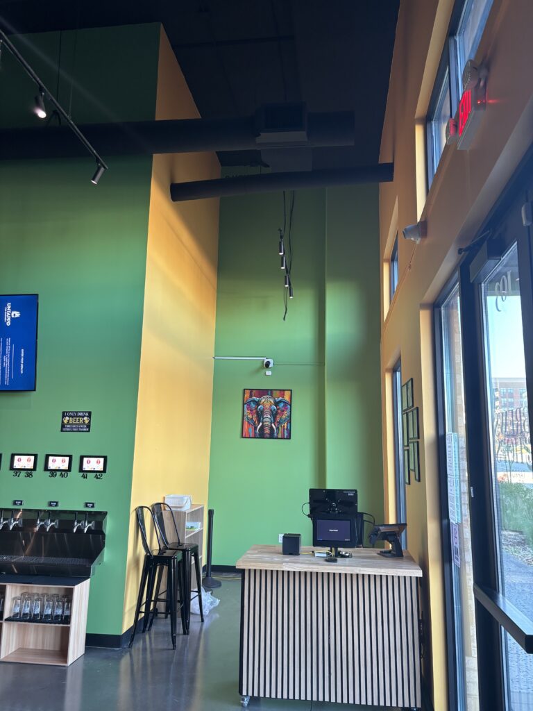 Interior corner of Brews and Hops taproom in Chamblee GA with tall windows green accent wall and exposed ceiling
