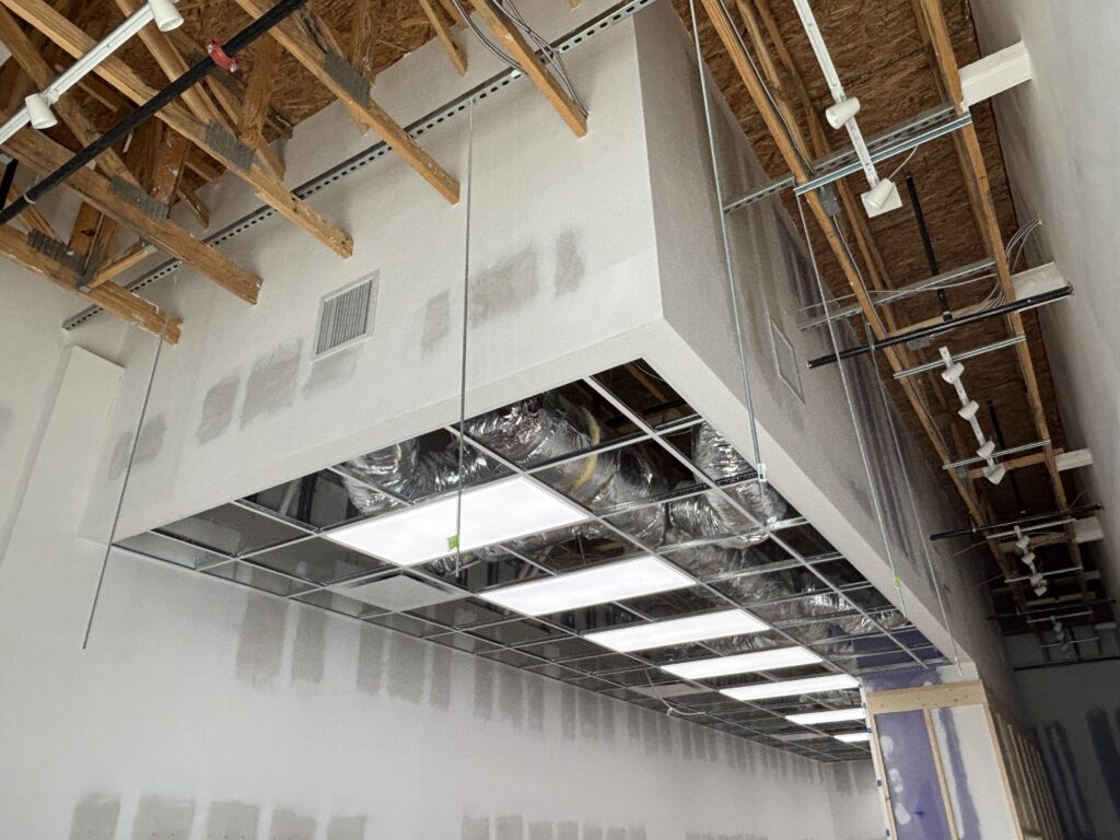 Offset soffit and in dining area with primed drywall walls exposed wood structure and recessed light openings