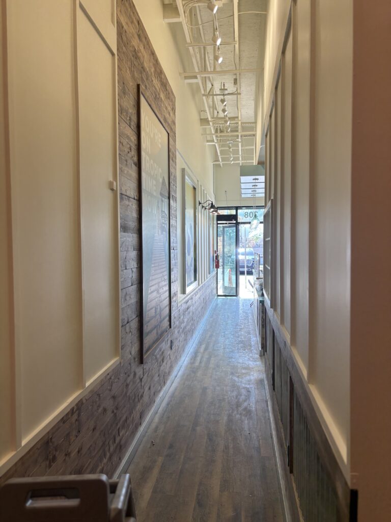 Finished corridor with stained decorative wood wall panels, luxury vinyl plank flooring, wall graphics, wood trim accents, and exposed ceiling systems