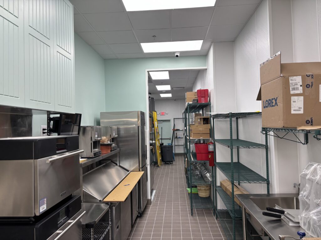 Commercial kitchen with quarry tile flooring, stainless steel worktables, shelving, and completed wall finishes